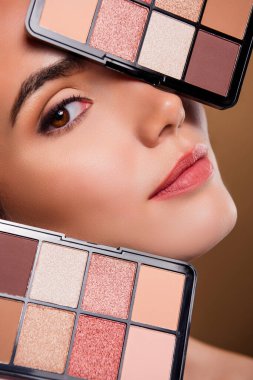 İhtiraslı, parlak kızın dikey fotoğrafı. Göz farı paletleri, izole edilmiş kahverengi arka plan..