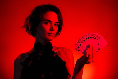 Çekici genç bir bayanın eski tarz elbise giyip VIP kumarhane klübünde kart tutarken çekilmiş fotoğrafı. Koyu kırmızı arka planda..