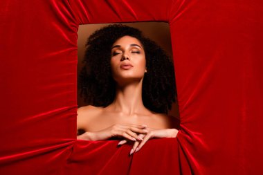 Kırmızı kadife duvarın arkasındaki delikli kenarda oturan çekici kadının fotoğrafı. Gözlerini kapat..