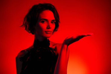 Eski moda güzellik ürünlerini sunan çekici bir kadının fotoğrafı koyu kırmızı arka planda izole edilmiş..