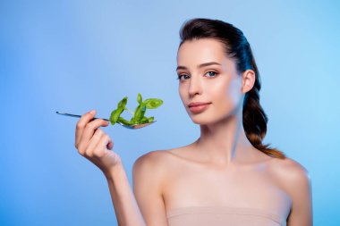 Biyolojik bitkilerle kaşık tutan güzel bir bayanın fotoğrafı izole edilmiş mavi arkaplan reklamları yapıyor..