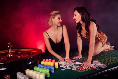 İki çapkın karizmatik kadının fotoğrafı baştan çıkarıcı elbiseler giyer. Siyah Jack Jackpot 'un izole edilmiş kırmızı duman arka planına takılır..