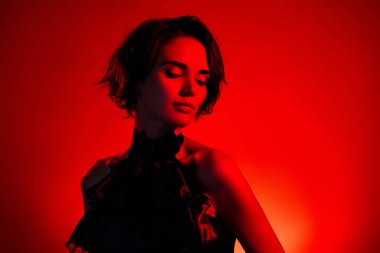 Kırmızı neon arka planda izole edilmiş cadılar bayramı partisini kutlayan zarif şık bir kadının fotoğrafı.