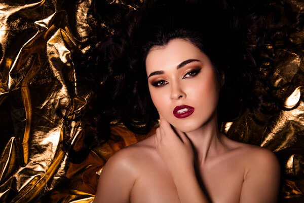 Фотография на фоне золотистой фольги очаровательной обнаженной девушки с идеальным макияжем.