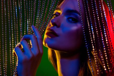 Göz kamaştırıcı, güzel bir bayanın elmas mücevher peçesine dokunuşunun fotoğrafı neon renkli arka planda baştan çıkarıcı bir his uyandırıyor..