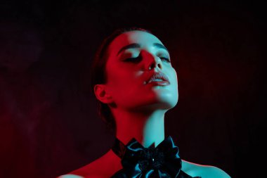 Çekici bir kızın fotoğrafı gotik bir retro giysi giyer gözleri koyu neon rengi arka planda cazip gelir..