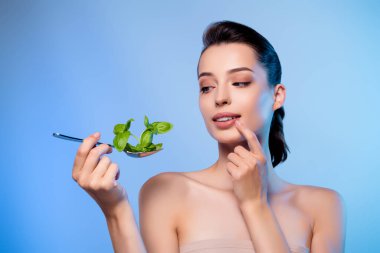 Çekici, güzel bir bayanın fotoğrafı. Elinde bitki yapraklarıyla kaşık tutarken ilginç mavi bir arkaplan olduğunu düşünüyor..