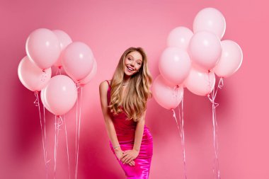 Pembe giyinmiş genç bir kadın pembe balonların arasında duruyor. Şenlikli bir ortamda cazibe ve incelik saçıyor..