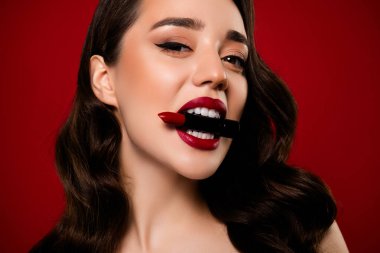 Kırmızı arkaplanda izole edilmiş maquillage uygulayan çarpıcı çekici modelin yakın plan fotoğrafı.