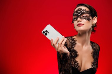 Çekici, genç ve yaşlı bir kızın fotoğrafı dantelli, siyah elbiseli, maskeli, Kraliçe kılık değiştirmiş kırmızı arka plan..