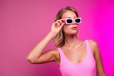 Güneş gözlüklü havuz partisine dokunan güzel bir bayan modelin fotoğrafı pembe renkli arka planda izole edilmiş bir vücut giysisi..