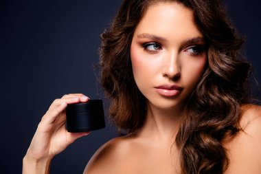 Çekici esmer kadın kozmetik kavanozuyla koyu gri bir zemin üzerinde poz veriyor, cazibe, güzellik ve lüks cilt bakımı..