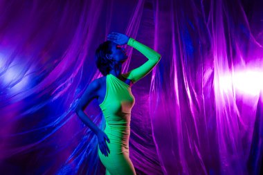 Güzel model kızın portresi mükemmel figürlü yeşil elbise. Neon stüdyo perde arkasında izole edilmiş..