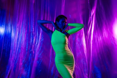 Güzel, kendine güvenen model kızın portresi neon stüdyo perde arkasında izole edilmiş yeşil bir elbise..