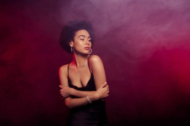 Şık, zarif bayanın fotoğrafı kendini kucaklıyor koyu kırmızı arka planda izole edilmiş konforun keyfini çıkarıyor..