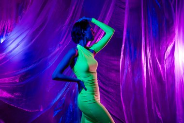 Güzel manken kızın el dokunuşunun fotoğrafı. Bele dokunmak. Neon stüdyo perde arkasında izole edilmiş yeşil elbise pozu..