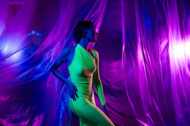 Neon stüdyo perde arkasında izole edilmiş yeşil elbiseli güzel kız dansının fotoğrafı..