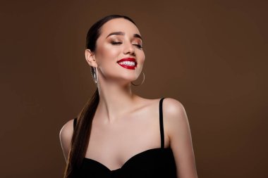 Tatlı tutkulu modelin fotoğrafı siyah elbise giy. Küpelerinin tadını çıkar. Boş alan, izole edilmiş kahverengi arka plan..