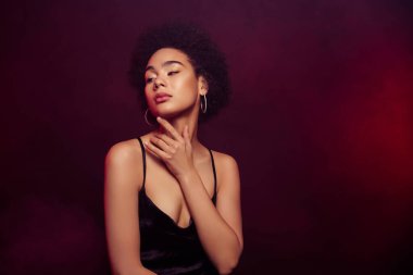 Mutlu, çekici, çarpıcı bir modelin fotoğrafı. Boyun teması. Burgonya rengi arka planda izole edilmiş siyah bir elbise..