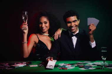 Zarif giyinmiş göz kamaştırıcı bir çift poker fişleri, kartlar ve şampanyalarla dolu bir kumarhane masasında eğleniyor..