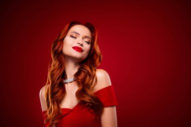 Kıvırcık, güzel, kızıl saçlı bir kızın fotoğrafı. Gözleri kapalı. Göz kamaştırıcı bir elbise giymekten zevk alıyor..