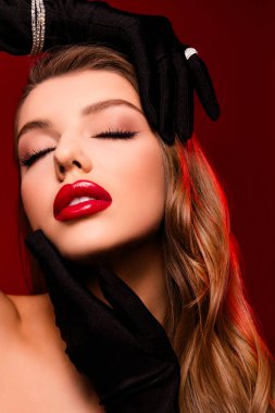 Parlak makyajlı güzel bir kadının fotoğrafı. Kapalı gözler. Kırmızı arka planda dokunaklı bir yüz..