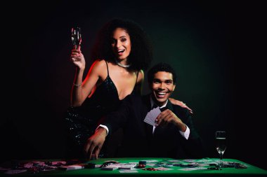 Havalı bir çift kumarhanede zarif bir akşamı kutluyor. Ellerindeki şampanyayla, lüks bir atmosferle çevrili kumar masalarının cazibesinin ve heyecanının tadını çıkarıyorlar..