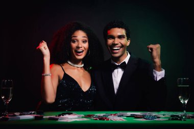 İki genç kumarhanede kazanmayı parlak gülümsemeyle kutluyor. Zarif çift, resmi giysiler içinde, oyun atmosferinin heyecanı ve cazibesinden zevk alır, mutluluk ve lüks saçar..