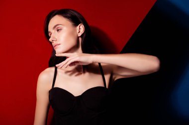 Zarif genç bir kadın zarif bir şekilde kırmızı ve siyah bir zemine karşı poz veriyor, zarafeti ve modern moda eğilimlerini temsil ediyor..