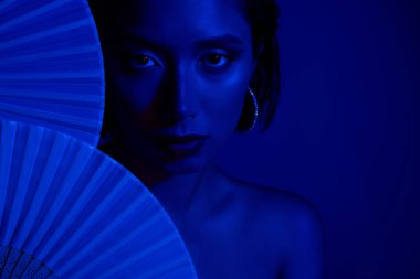 Çinli kağıt hayranlarının arkasına saklanan sevimli kadının fotoğrafı. Boş uzay mavisi arka plan..