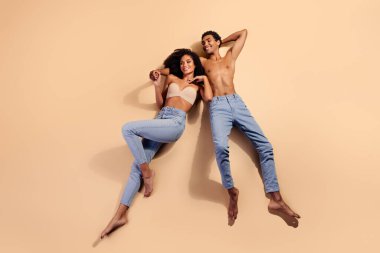 Genç bir çift, bej renkli bir stüdyo arka planında gülümseyen, sevgi, güzellik ve doğal bir bağ gösteren neşeli bir anın tadını çıkarır..