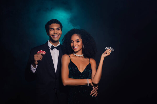 Элегантная пара в казино ночью, проведение фишки для покера на темном фоне, источая гламур и изысканность.