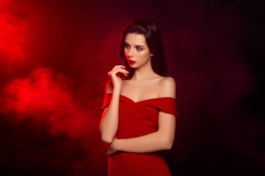 Kırmızı elbiseli genç bir kadının şık bir portresi, özgüven ve zarafet sergiliyor, sanatsal ışıklandırma ve dumanlı efektlerle büyüleyici bir atmosfer yaratıyor..