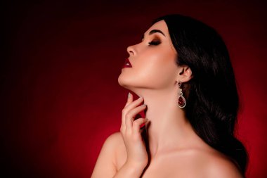 Güzel model bir kadının profil portresi. Elini boynuna değdir. Koyu kırmızı arka planda izole edilmiş boş bir alan..