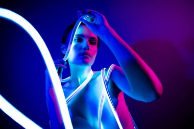 Neon ışıkla kaplanmış, koyu mavi arka planlı, modern moda görünümünü vurgulayan büyüleyici bir kadın görüntüsü..