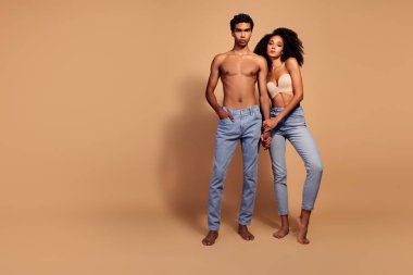 Bej renkli stüdyo geçmişine karşı kot modasında birlikte poz veren çekici genç bir çift..