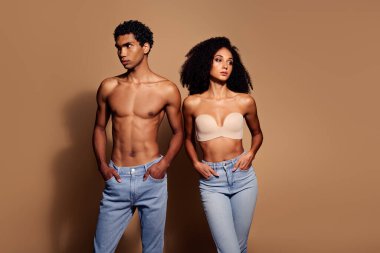 Kot pantolon ve iç çamaşırı giyen çekici genç bir çift stüdyoda güven içinde poz veriyor. Sıcak bej arka plan, doğal güzelliklerini ve tarzlarını vurgular..