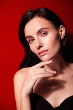 Cesur kırmızı bir altyapının önünde zarif bir kadın zarif duruşu ve düşünceli ifadesiyle vurgulanmış sofistike ve güzel bir görünüm sergiler..