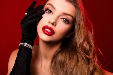 Göz kamaştırıcı bir kadının fotoğrafı siyah eldivenlerle yüzüne dokunuyor. Kırmızı arka planda parlak dudakları var..