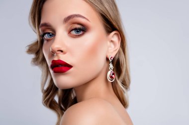 Gri arkaplandan kameraya bakan kırmızı yakut yakut değerli küpeli çekici kız..