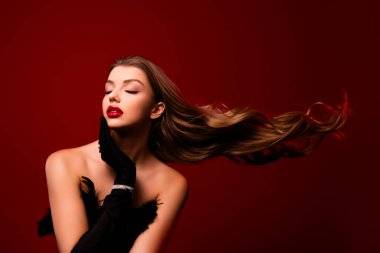 Göz kamaştırıcı bir kadın yumuşak yumuşak yumuşak bir cilt dokunuşu siyah eldivenlerle kırmızı arka planda kapalı gözler.