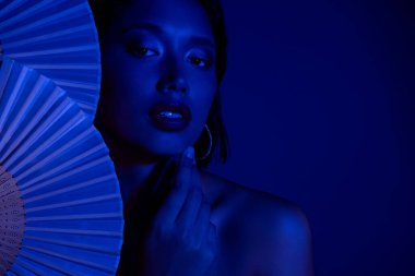 Japon kağıt yelpaze tutan narin, parlak bir bayanın fotoğrafı tenha, tenha, mavi arka plana dokunuyor..