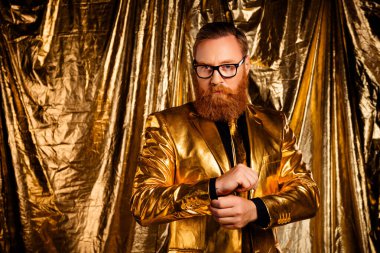 Göz kamaştırıcı altın takım elbiseli şık bir adam ışıldayan bir arka planın önünde duruyor, entelektüellik ve tarz yayıyor. Şenlikli zarafet ve cazibeyi resmetmek için mükemmel..