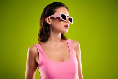 Güneş gözlüğü takan göz kamaştırıcı bir kızın fotoğrafı yeşil boş arkaplanda profil kenarına bak..