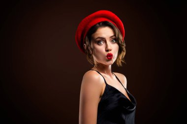 Fransız motifli şık bir kadın zarif poz veriyor, parlak kırmızı beresini, göz alıcı kırmızı rujunu ve zarif siyah elbisesini sergiliyor..