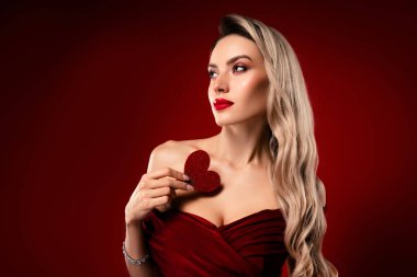 Güzel, sarışın bir kadın zarif bir şekilde kırmızı giyinmiş ve sembolik bir kalp dekorasyonuyla cazibesini göstermiş, entelektüel ve cazibeli.