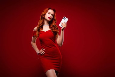 Kokteyl elbisesi giymiş klas bir kızın fotoğrafı. Kırmızı arka planda cep telefonu şaklabanlığı kullan..
