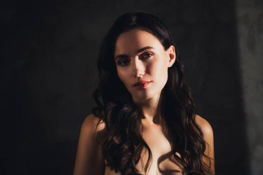 Dalgalı kıvırcık saçlı hoş bir bayanın portresi. Karanlık arka planda güneş ışığına bakıyor..