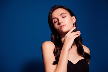 Zarif bir kadın, gözleri kapalı, zarif ve kültürlü, zarif mücevherlerle süslenmiş. Parlak mavi arka plan onun huzurlu ifadesini arttırıyor..