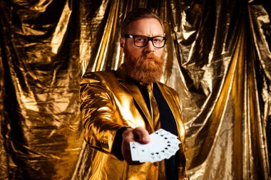 Kırmızı sakallı ve gözlüklü karizmatik bir adam, altın takım elbiseli, lüks bir geçmişi olan yetenekli bir adam..